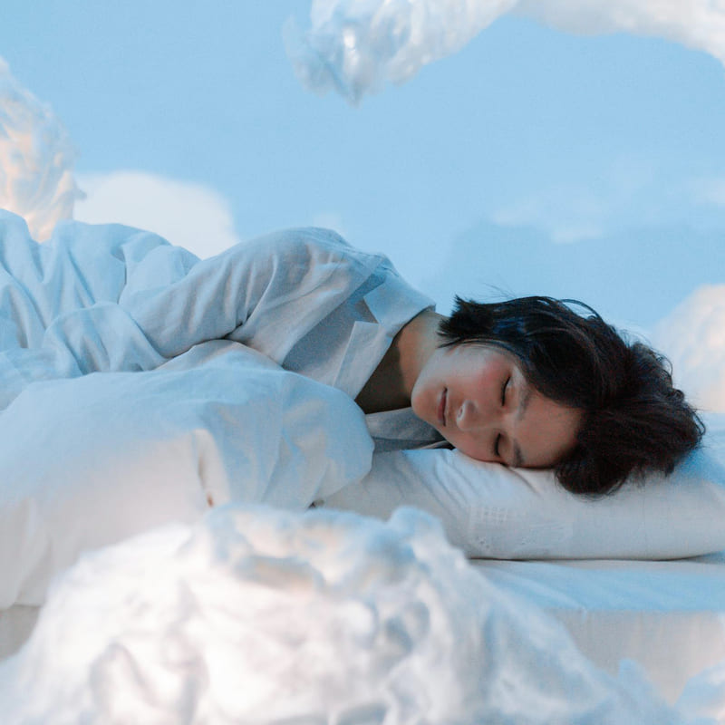 Femme qui dort dans un lit avec des nuages autour pour évoquer le sommeil. Version mobile