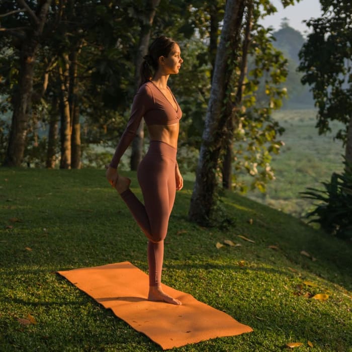 Femme faisant du yoga sur un tapis orange avec un fond végétal. Elle a l'air détendu. Cette image fait référence au patch stress